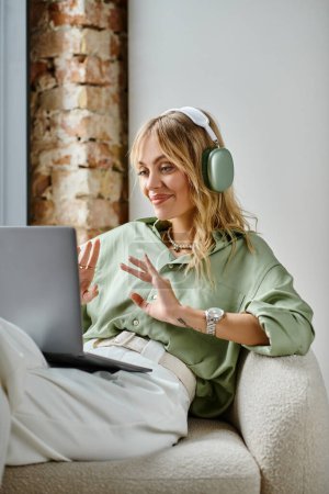 Photo for A woman in headphones sitting on a couch in a cozy apartment. - Royalty Free Image