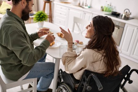 Photo for Good looking jolly man enjoying breakfast with his disabled merry wife in wheelchair at breakfast - Royalty Free Image