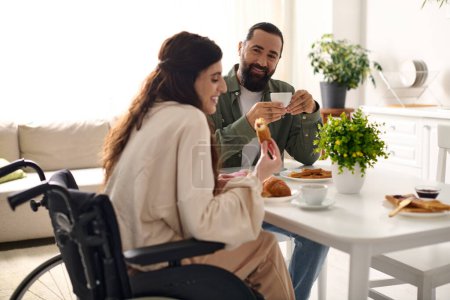 Téléchargez les photos : Homme positif avoir beaucoup de temps au petit déjeuner avec sa belle femme handicapée qui mange croissant - en image libre de droit