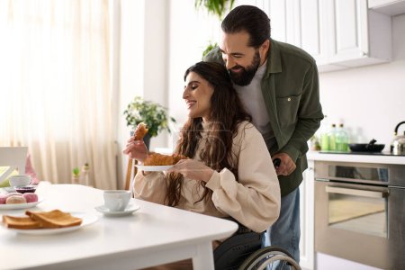 Téléchargez les photos : Homme joyeux ayant beaucoup de temps au petit déjeuner avec sa belle femme handicapée qui mange croissant - en image libre de droit