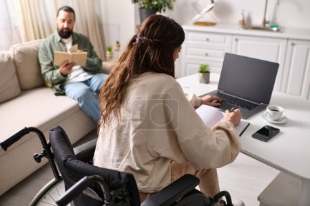 Behinderte Frau im Rollstuhl arbeitet von zu Hause aus am Laptop neben ihrem lesenden Mann