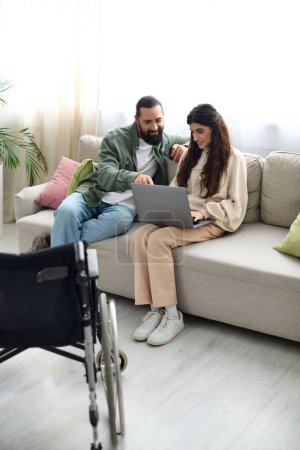 schöne Frau mit Gehbehinderung sitzt auf Sofa mit Laptop neben ihrem Mann mit Telefon