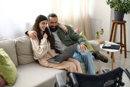 loving couple of bearded man and disabled beautiful wife spending time together at laptop on sofa