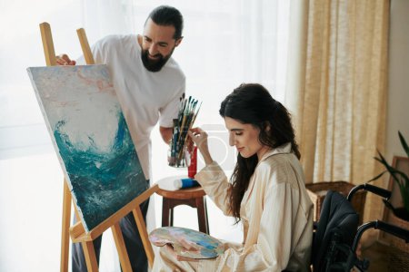 Photo for Loving cheerful couple of bearded man and disabled woman painting on easel together at home - Royalty Free Image