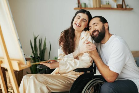 Foto de Atractiva mujer con discapacidad de movilidad pintura en caballete junto a su alegre marido barbudo - Imagen libre de derechos