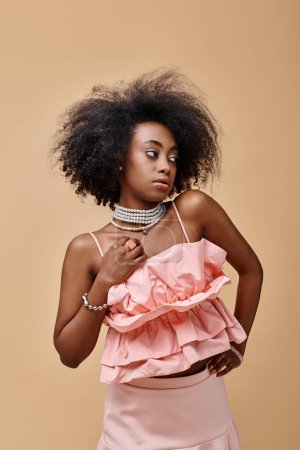 dreamy african american girl in 20s posing in peach ruffle top and pastel skirt on beige backdrop