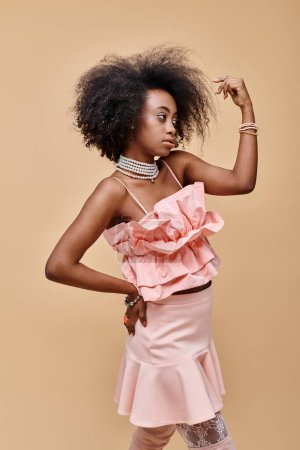 dreamy african american girl in 20s posing in peach ruffle top and pastel skirt with hand on hip