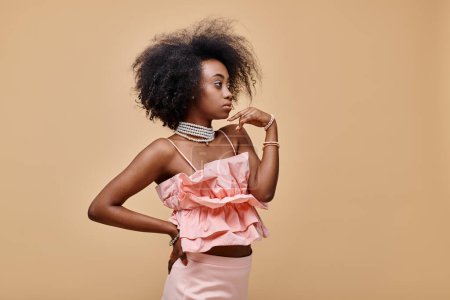 pretty african american girl in 20s posing in peach ruffle top and pastel skirt with hand on hip