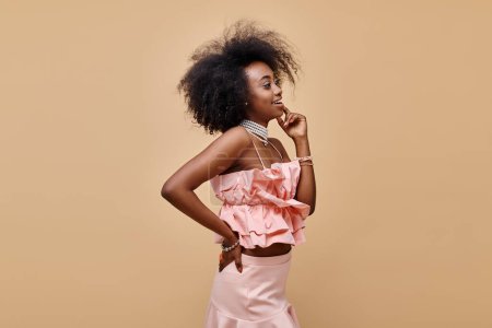 happy african american girl in 20s posing in peach ruffle top and pastel skirt with hand on hip
