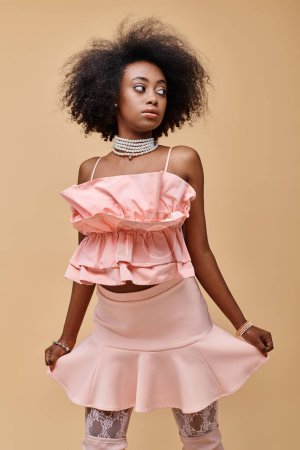 Photo for Pretty dark skinned model with curly hair posing in pastel peach ruffled top on beige background - Royalty Free Image
