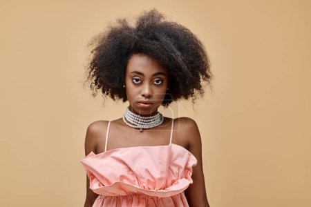pretty dark skinned woman with curly hair posing in pastel peach ruffled top on beige background