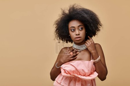 young dark skinned woman with curly hair posing in pastel peach ruffled top on beige background