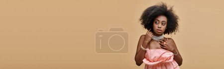 Banner einer hübschen dunkelhäutigen Frau mit lockigem Haar posiert in pfirsichfarbenem Rüschenoberteil auf beigem Hintergrund