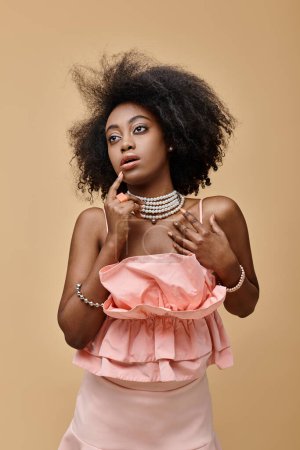 dreamy dark skinned woman with curly hair posing in pastel peach ruffled top on beige background