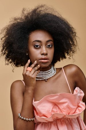 portrait of dark skinned woman with curly hair posing in pastel ruffled top on beige backdrop, peach