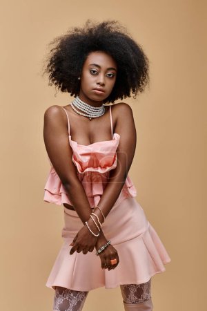 young dark skinned model with curly hair posing in pastel peach ruffled top on beige background