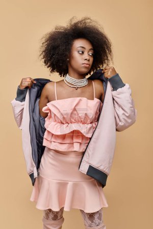 african american girl in 20s, posing in peach outfit with jacket on beige background, color of year