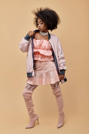 Foto de Chica afroamericana de 20 años, posando en traje de melocotón con chaqueta y botas sobre la rodilla en beige, 2024 - Imagen libre de derechos