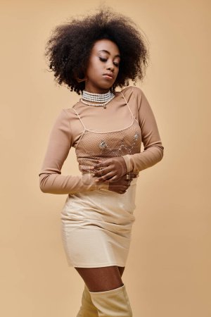 young african american woman with curly hair posing in stylish pastel outfit on a beige backdrop