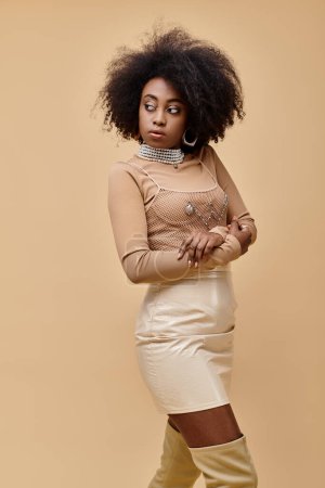 junge Afroamerikanerin mit lockigem Haar posiert im pastellfarbenen Pfirsich-Outfit auf beigem Hintergrund