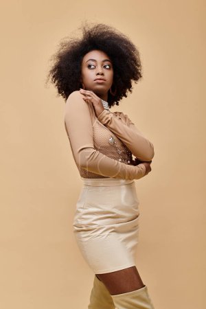 chica joven afroamericana con el pelo rizado posando en traje de melocotón pastel sobre fondo beige