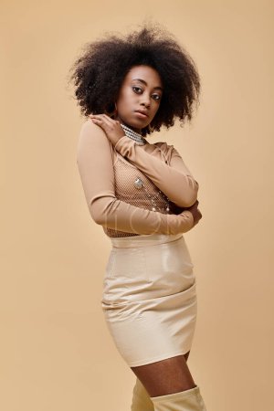 young african american model with curly hair posing in pastel peach outfit on beige backdrop