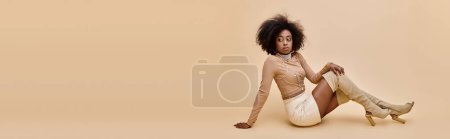 african american girl in trendy outfit and thigh-high boots reclines on beige backdrop, banner