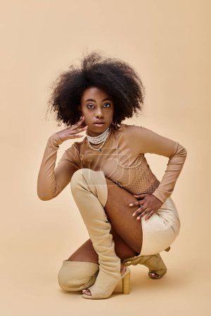curly african american model in trendy peach fuzz outfit and thigh-high boots sitting on a beige