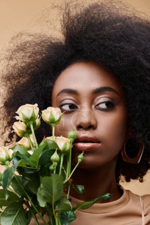 dreamy curly african american woman holding tiny roses on beige background, peach fuzz color