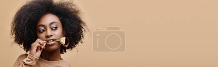 Foto de Mujer americana africana rizada con pequeña rosa en los dientes sobre fondo beige, pancarta de pelusa de melocotón - Imagen libre de derechos