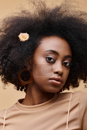 sensual young african american girl with small rose in curly hair on beige background, peach fuzz