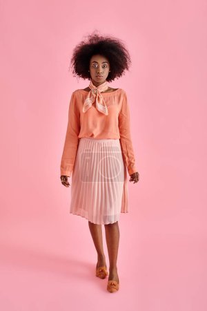 Photo for Graceful african american woman in peach blouse and midi skirt posing on pastel pink background - Royalty Free Image