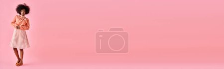 Téléchargez les photos : Femme afro-américaine bouclée en chemisier pêche et jupe midi frappe une pose sur rose pastel, bannière - en image libre de droit