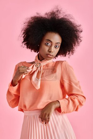 Photo for Young african american woman in peach blouse adjusting neck scarf and posing on pink background - Royalty Free Image