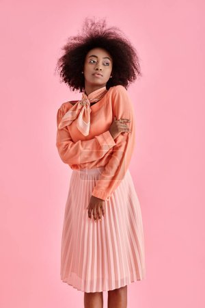 Photo for Curly african american woman in peach blouse, midi skirt and neck scarf posing on pink background - Royalty Free Image