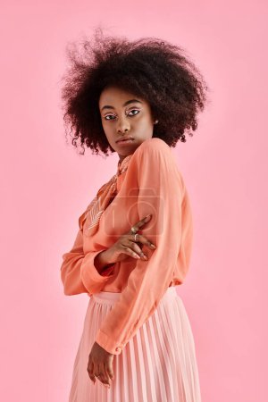 Selbstbewusste Afroamerikanerin in Pfirsichbluse, Midirock und Halstuch posiert auf rosa Hintergrund