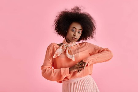 hübsche Afroamerikanerin in pfirsichfarbener Bluse, Midirock und Halstuch posiert auf rosa Hintergrund