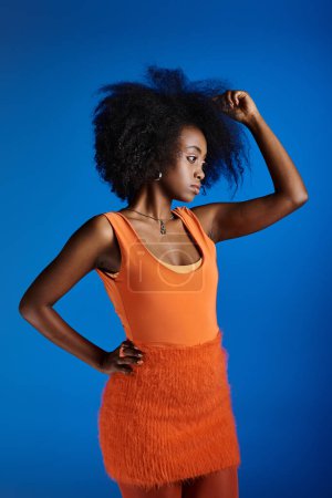 Photo for Curly african american woman in textured dress posing with hand on hip on vivid blue backdrop - Royalty Free Image