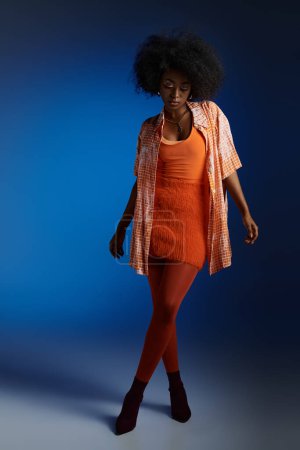 Schicker Look einer jungen Afroamerikanerin in gemustertem Hemd und orangefarbenem Kleid auf blauem Hintergrund