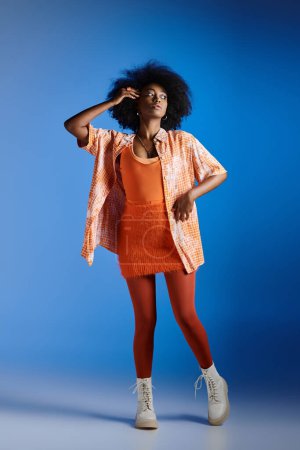 modisches afrikanisch-amerikanisches Model in gemustertem Hemd und strukturiertem Kleid posiert auf blauem Hintergrund