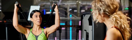 entrenador femenino deportivo consultando a su cliente alegre rubia en el gimnasio cerca de hombro máquina de prensa, pancarta