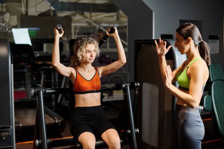 sportliche brünette weibliche Trainerin berät ihren blonden freudigen Kunden im Fitnessstudio in der Nähe der Schulterpresse