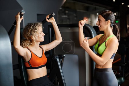 starke weibliche Trainerin berät ihre attraktive, freudige Kundin im Fitnessstudio in der Nähe der Schulterpresse