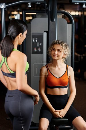 Photo for Joyful female coach explaining to her appealing jolly client how to use chest press machine - Royalty Free Image