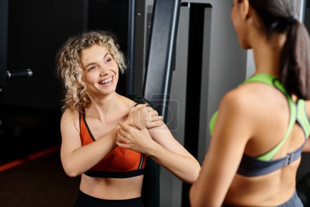 Photo for Cheerful female coach explaining to her appealing jolly client how to use chest press machine - Royalty Free Image