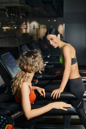 joyous appealing female coach and her client in sportwear exercising actively on treadmill in gym