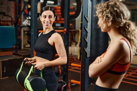 fröhliche, gut aussehende Frau und ihre athletische Trainerin beim Training mit Powerbag im Fitnessstudio