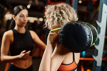 attractive sporty woman and her athletic female coach practicing with power bag while in gym