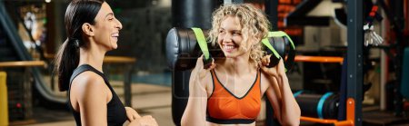happy beautiful woman and her athletic female coach practicing with power bag while in gym, banner