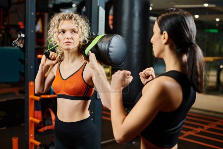 beautiful sporty woman and her athletic female coach practicing with power bag while in gym